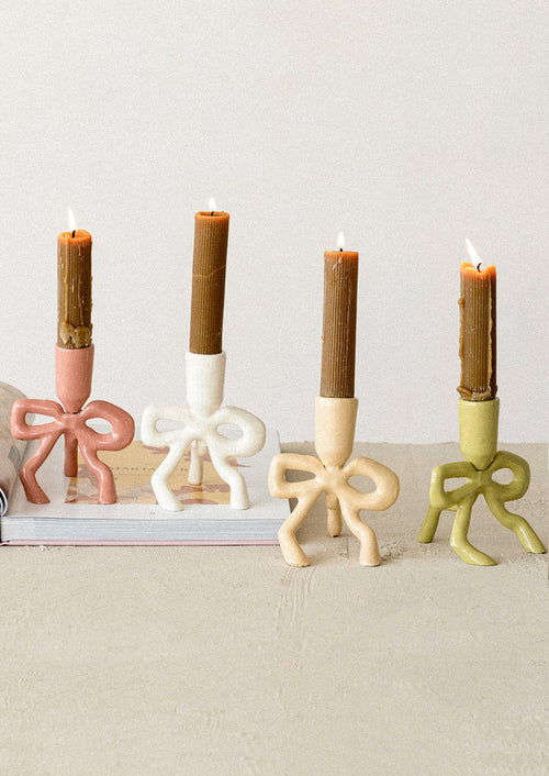 Four bow-shaped candle holders with candles on a neutral background